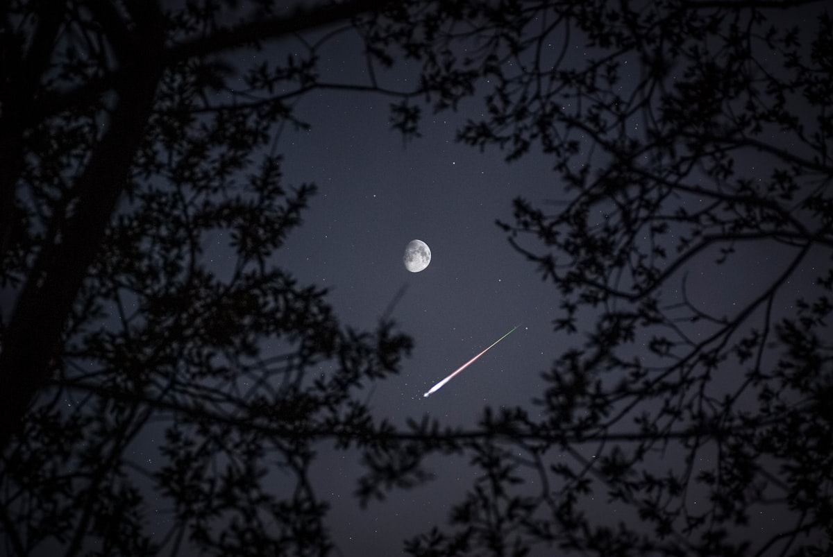 Meteor streak below the moon in a night sky — illustrating unpredictable risk events