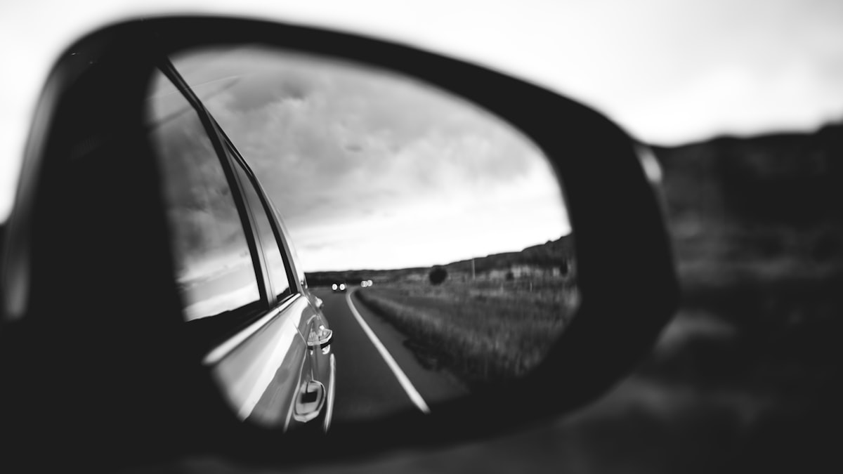 Car side mirror reflecting a road stretching into the distance &mdash; looking backwards through regulation